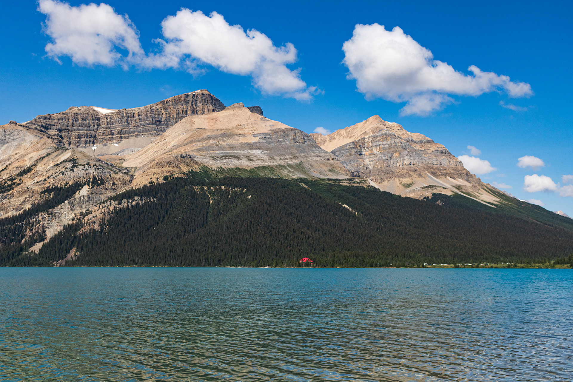 Lake with a large rocky mountain behind it and trees at its foundation.